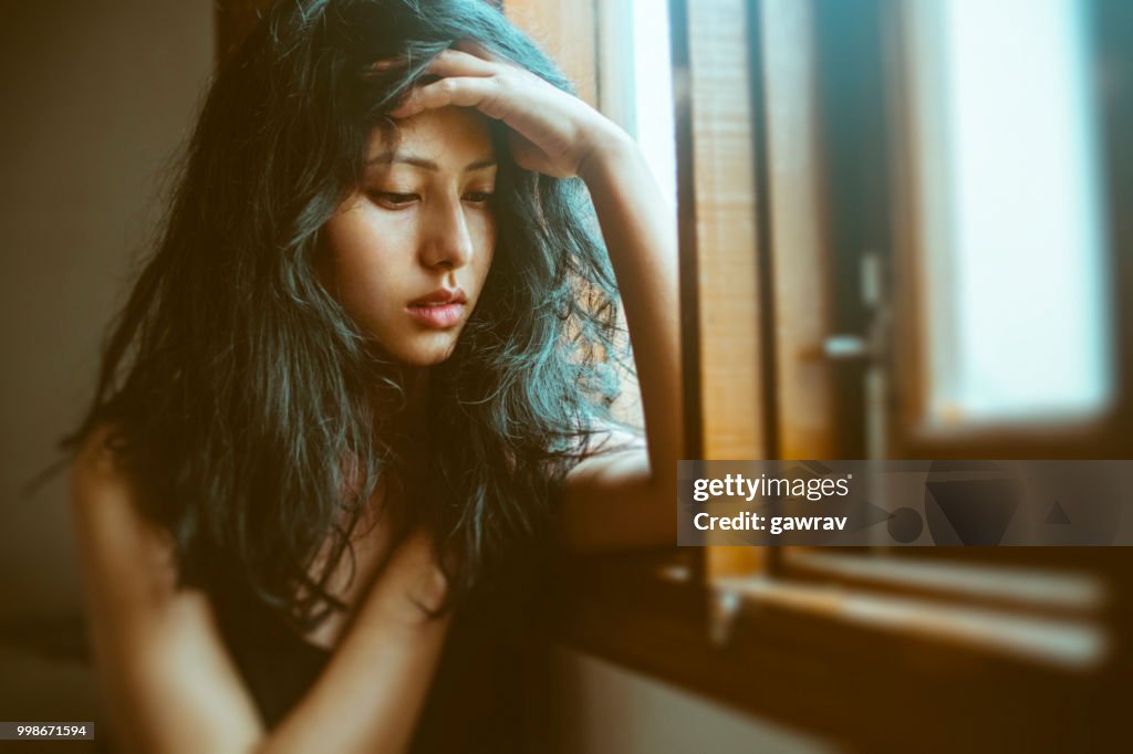 Sad young woman thinks near window.