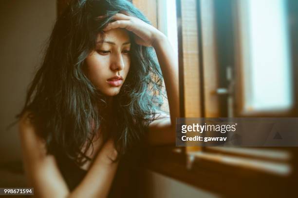 sad young woman thinks near window. - loneliness stock pictures, royalty-free photos & images