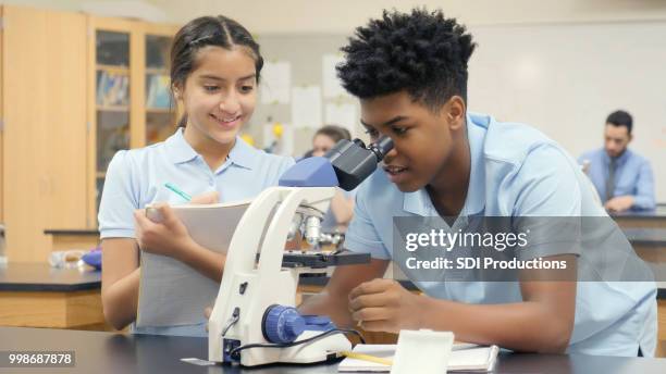 teen boy usa il microscopio nella classe di scienze scolastiche - educazione di scuola privata foto e immagini stock