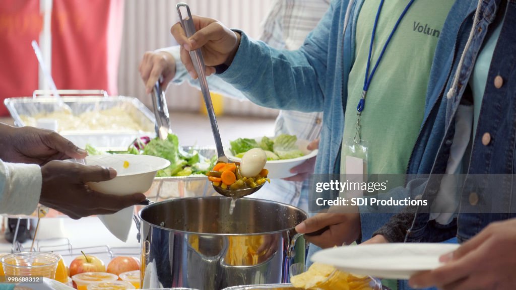 Unrecognizable volunteer serves soup in soup kitchen