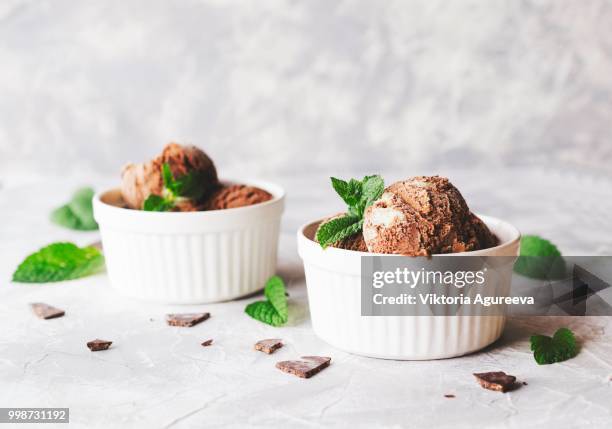 chocolate mint ice cream in white bowls with pieces of chocolate and mint leaves on a marble table - mint ice cream stock pictures, royalty-free photos & images