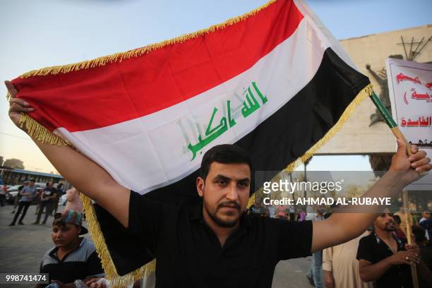 An Iraqi man carries the national flag as he demonstrates in the capital Baghdad's Tahrir Square against unemployment on July 14, 2018. - Two...