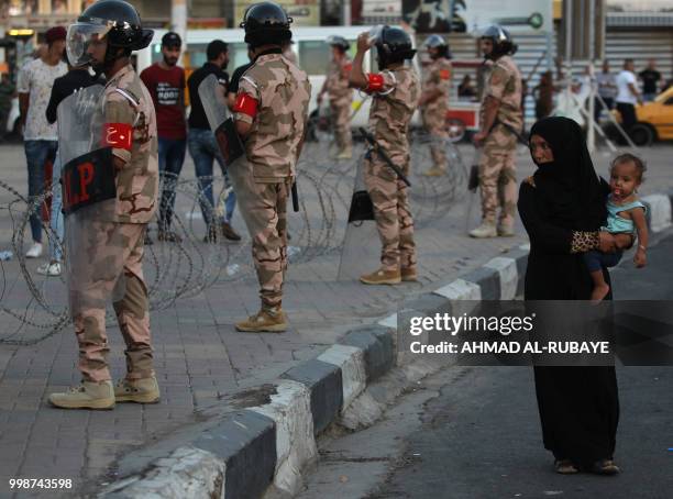 Woman walks near Iraqi security forces standing guard in the capital Baghdad's Tahrir Square, during demonstrations against unemployment on July 14,...