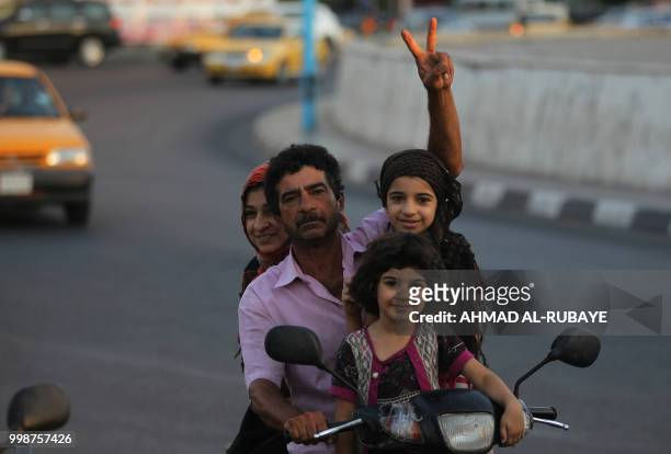 An iraqi man transporting his family on a motorbike flashes the victory sign in the capital Baghdad's Tahrir Square during demonstrations against...