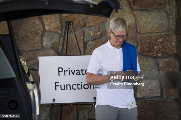 Tim Cook, chief executive officer of Apple Inc., uses an Apple iPhone X while waiting for a car after the morning session at the Allen & Co. Media...