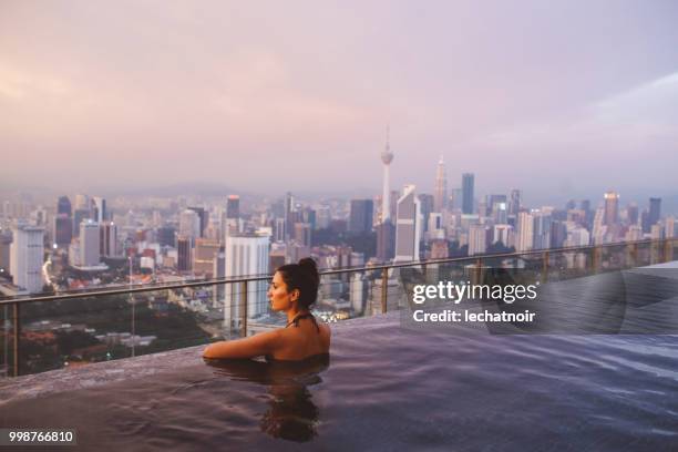 jovem morena relaxando na piscina como o sol se põe acima de kuala lumpur, malásia - infinity pool - fotografias e filmes do acervo