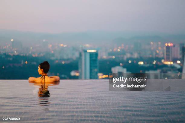 jeune femme relaxante dans la piscine sous le soleil se couche au-dessus de kuala lumpur - piscine à débordement photos et images de collection