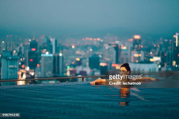 young woman relaxing in the pool as the sun sets above kuala lumpur - kuala lumpur stock pictures, royalty-free photos & images