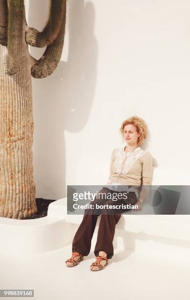 young woman sitting against white wall - bortes stock-fotos und bilder