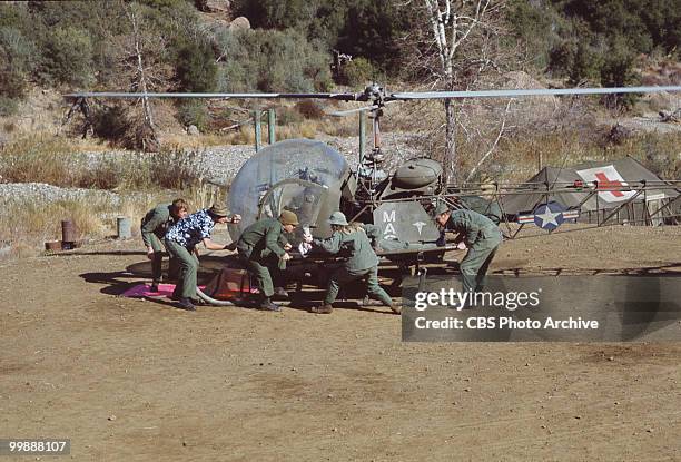 Cast members crouch under the propeller blades of a helicopter in a scene from the television series 'MASH,' California, 1974.