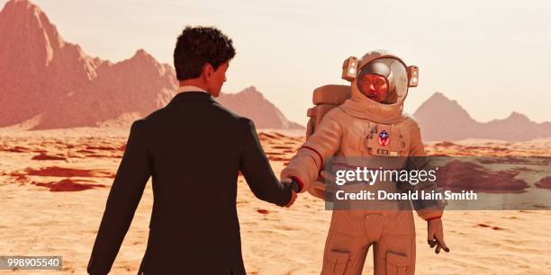 business man shaking hands with astronaut in red desert landscape - astronaut hand stock pictures, royalty-free photos & images