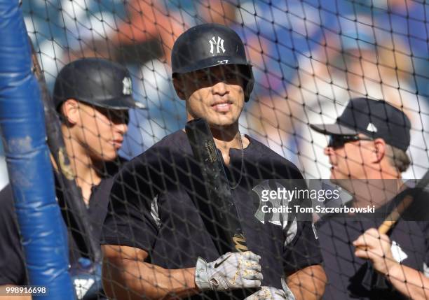 Giancarlo Stanton of the New York Yankees watches from outside the batting cage as Aaron Judge talks to third base coach Phil Nevin behind him during...