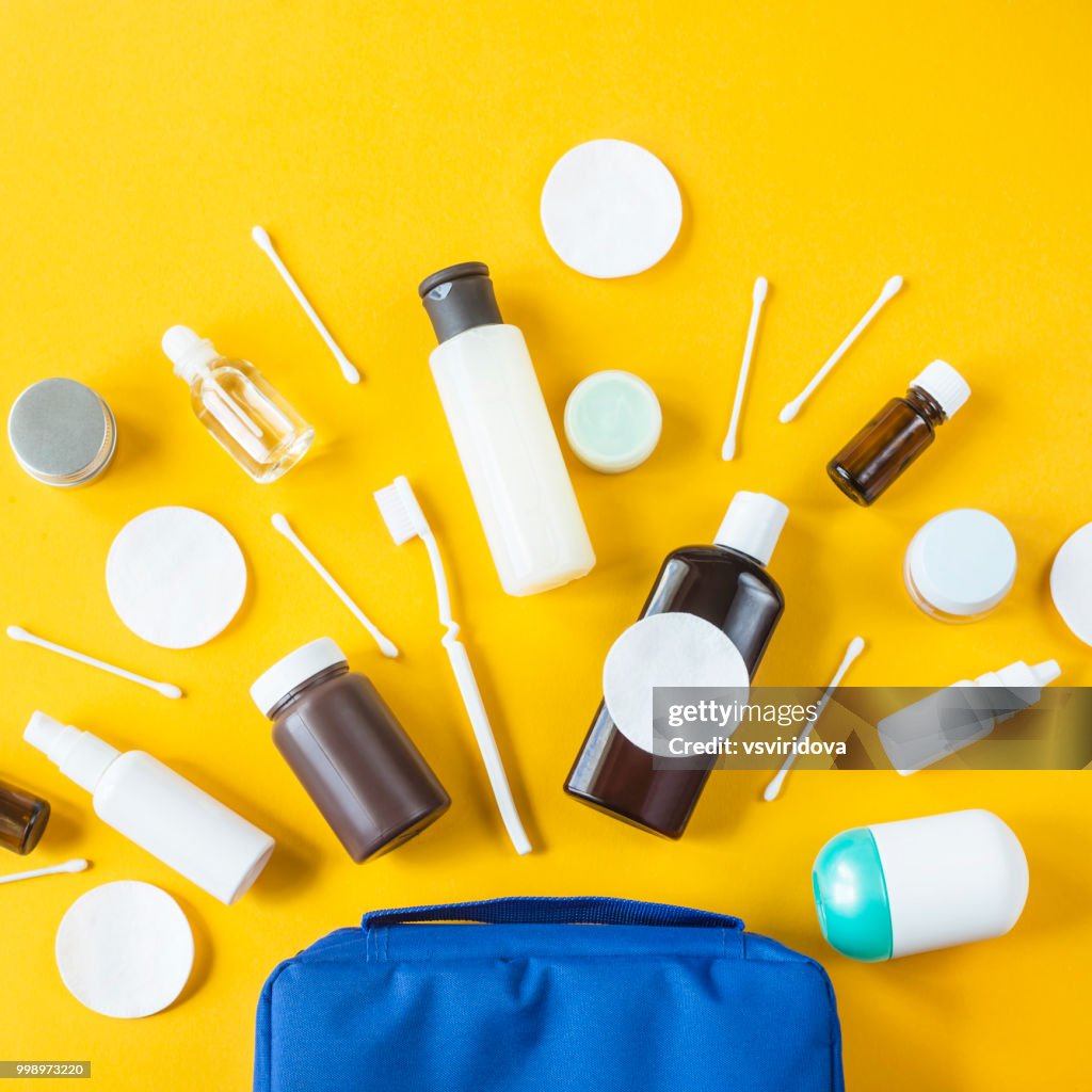 Jars and containers with cosmetics and cotton buds with disks from a blue cosmetic bag on a yellow background. Top view, flat lay