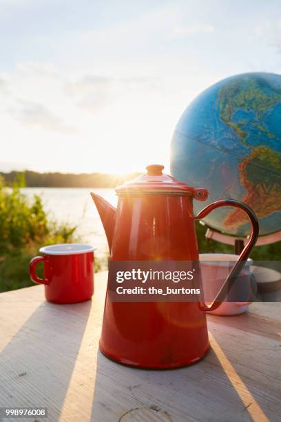 enamel pot, mugs and globe on a table at lakeside against sky and sunset - worldwide day of play and the carmelo anthony foundation san juan puerto rico stockfoto's en -beelden