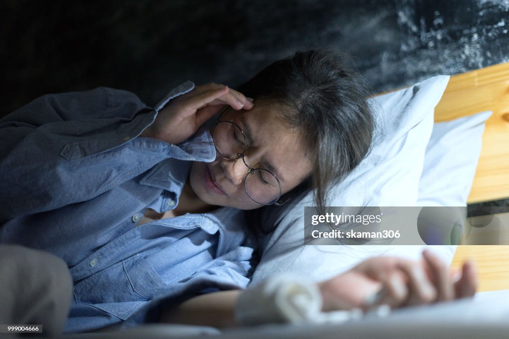 Asian female feeling sick and hand holding medicine tablet on the bed in the night time