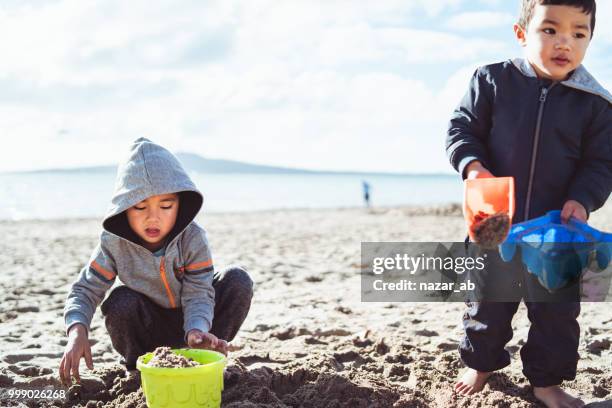 dos niños jugando con arena en la playa. - nazar fotografías e imágenes de stock