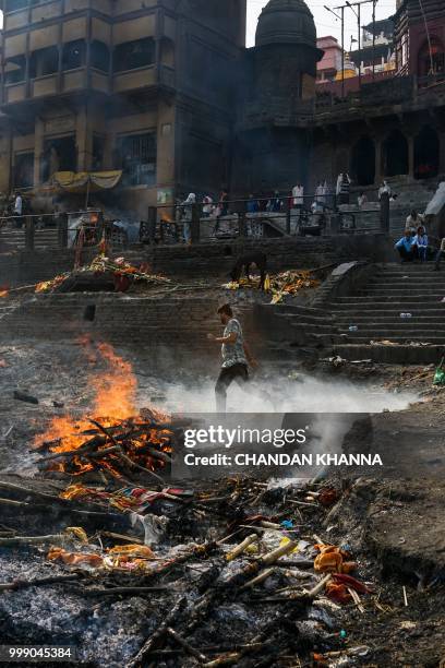This photo taken on June 2, 2018 shows an Indian man running past a funeral pyre at the Manikarnika ghat in the old quarters of Varanasi. - The Doms...