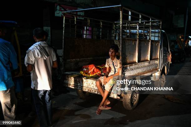 This photo taken on June 2, 2018 shows an Indian boy sitting on a van with the dead body of a relative at the Harishchandra ghat in the old quarters...