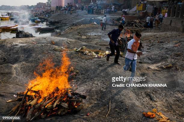 This photo taken on June 2, 2018 shows Indian men running past a funeral pyre at the Manikarnika ghat in the old quarters of Varanasi. - The Doms are...