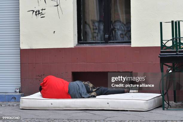 Man sleeps on an old mattress lying in the street in the Kruezberg borough of Berlin, Germany, 13 August 2017. Photo: Paul Zinken/dpa