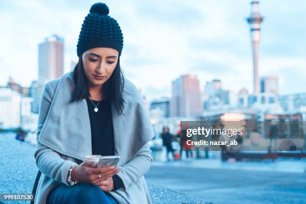 checking social media on phone with auckland city in background. - human migration stock pictures, royalty-free photos & images