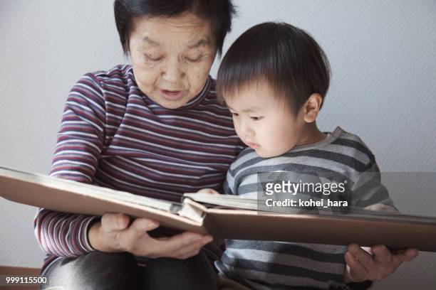 nonna e nipote guardano insieme un album fotografico - kohei hara foto e immagini stock
