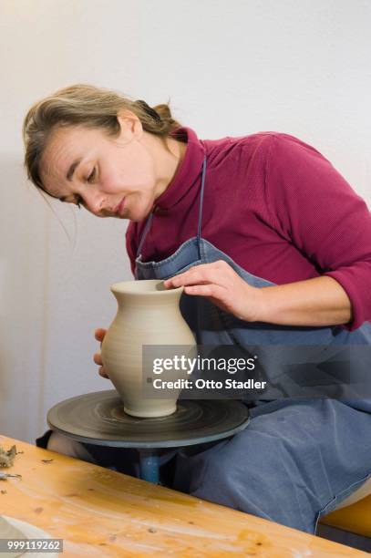 ceramic artist working in her workshop with a potter's wheel, polishing the surface of a pitcher, geisenhausen, bavaria, germany - tradesman fotografías e imágenes de stock