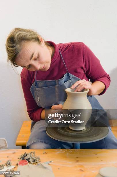 ceramic artist working in her workshop with a potter's wheel, polishing the surface of a pitcher, geisenhausen, bavaria, germany - bricolage stockfoto's en -beelden
