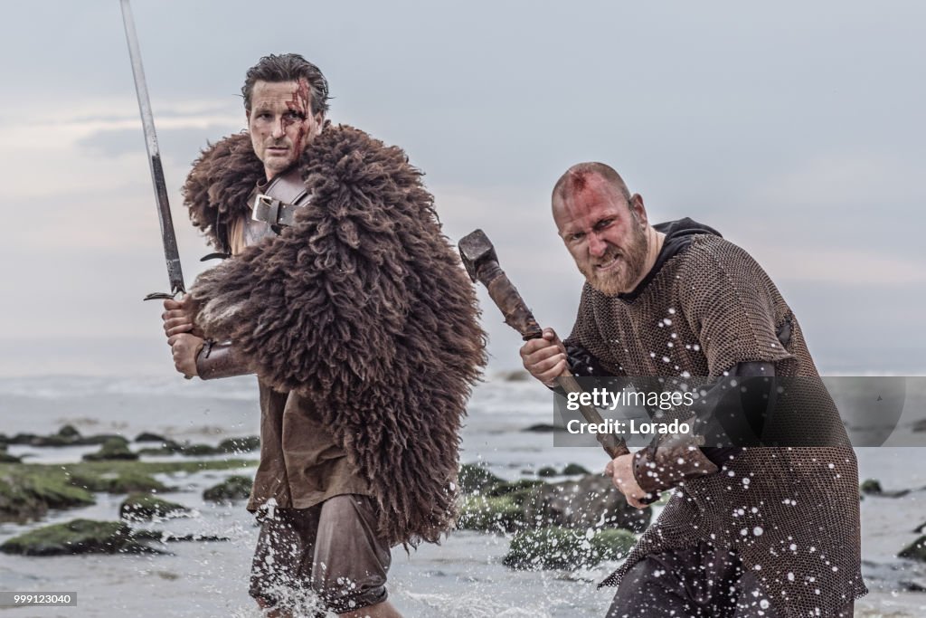 Two sword wielding bloody medieval warriors together on a cold seashore