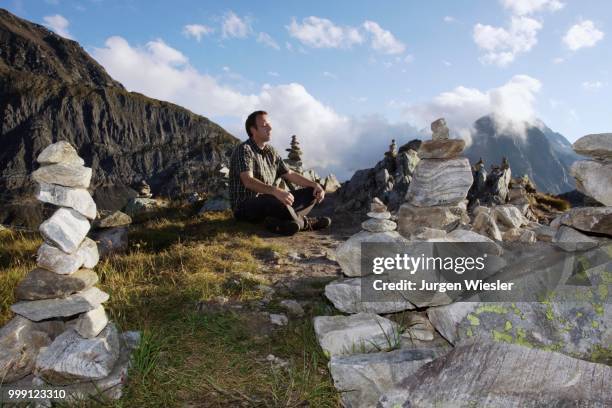 a man meditating between cairns on the nufenenpass at 2478m, canton valais, switzerland - valais canton photos et images de collection