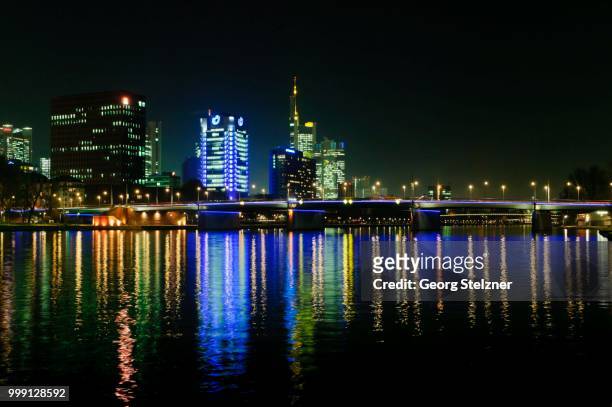 view of the frankfurt skyline with blue-lit union investment building, the yellow-lit commerzbank tower, ig metall headquarters, life at front, and friedensbruecke, from the south-west bank of the main river at night, frankfurt am main, hesse, germany - metall fotografías e imágenes de stock