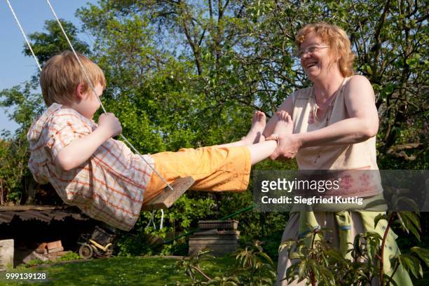 woman pushing a little boy on a swing - older woman younger man stock-fotos und bilder