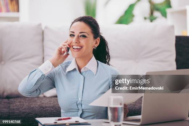 woman using laptop at home while talking on mobile phone - emir memedovski stock pictures, royalty-free photos & images