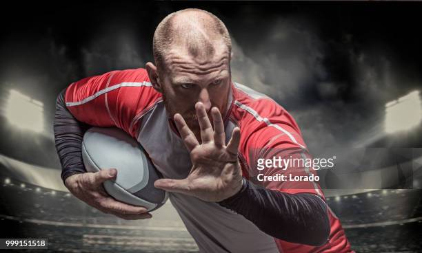 bearded aggressive redhead adult man rugby player holding a rugby ball in a floodlit stadium - rugby league stock pictures, royalty-free photos & images