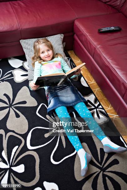 girl reading at home, germany - a woman modelling a trouser suit blends in with a matching background of floral print cushions stockfoto's en -beelden