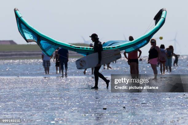 June 2018, Germany, Norddeich: A kitesurfer walking past other visitors with a kite and board on a beach on the North Sea. Photo: Mohssen...