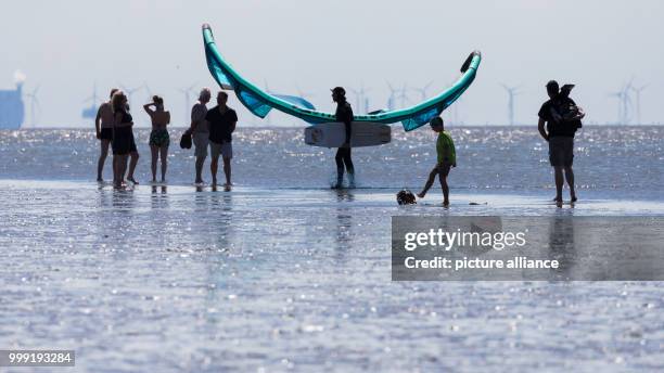 June 2018, Germany, Norddeich: A kitesurfer walking past other visitors with a kite and board on a beach on the North Sea. Photo: Mohssen...