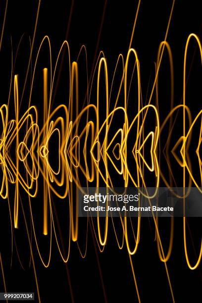 close-up abstract pattern of intertwined colorful light beams of colors yellow and gol colored on a  black background. - bernat bacete stock-fotos und bilder