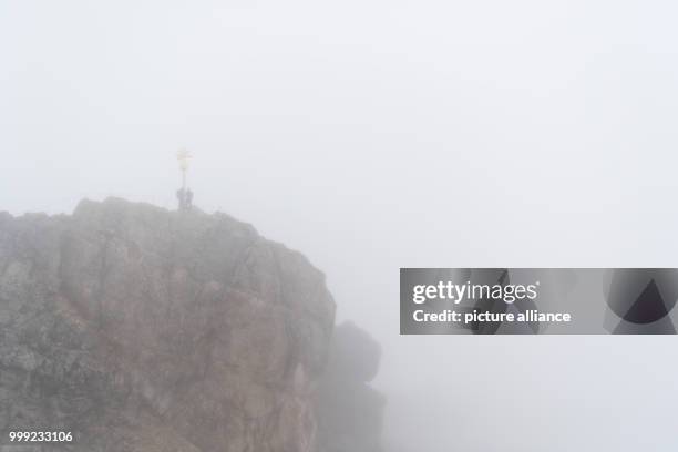 Two mountaineers stand next to the summit cross in the rain and fog at the Zugspitze in Grainau, Germany, 19 August 2017. Photo: Sven Hoppe/dpa