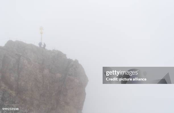 Two mountaineers stand next to the summit cross in the rain and fog at the Zugspitze in Grainau, Germany, 19 August 2017. Photo: Sven Hoppe/dpa