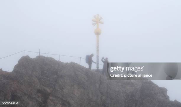 Two mountaineers stand next to the summit cross in the rain and fog at the Zugspitze in Grainau, Germany, 19 August 2017. Photo: Sven Hoppe/dpa
