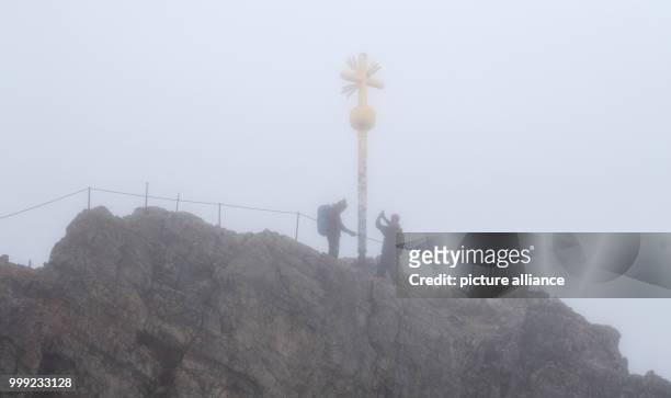 Dpatop - Two mountaineers stand next to the summit cross in the rain and fog at the Zugspitze in Grainau, Germany, 19 August 2017. Photo: Sven...