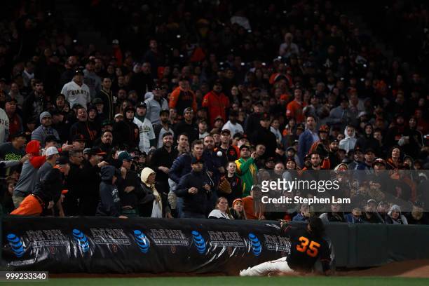 Brandon Crawford of the San Francisco Giants slides towards a barrier as he attempts to make a fly ball during the sixth inning against the Oakland...