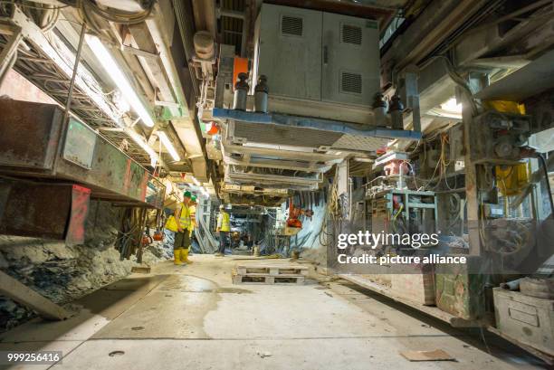 Three people walking past the front section of the tunnel drilling machine in a section of construction site for the Brenner Base Tunnel near...