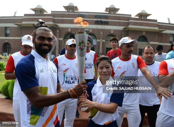 Indian hockey team captain Sreejesh Raveendran receives the torch from Indian boxer Mary Kom during the 2018 Asian Games torch relay in New Delhi on...