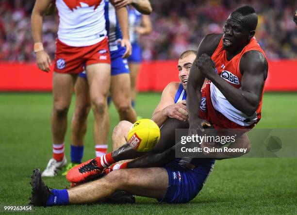 Aliir Aliir of the Swans handballs whilst being tackled by Ben Cunnington of the Kangaroos during the round 17 AFL match between the North Melbourne...