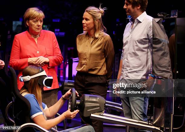 German chancellor Angela Merkel stands behind a gamer wearing Virtual Reality glasses during a presentation of a racing game at the Gamescom in...