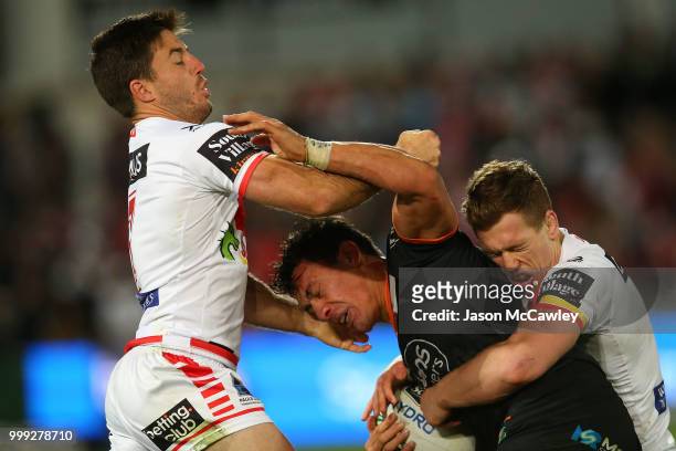 Elijah Taylor of the Tigers is tackled by Ben Hunt and Cameron McInnes of the Dragons during the round 18 NRL match between the St George Illawarra...