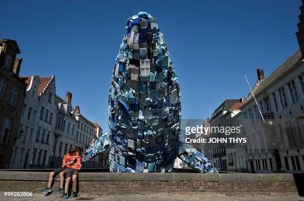 Children sit near a 12-metre installation depicting a whale, made up of five tons of plastic waste pulled out of the Pacific Ocean, is displayed in...