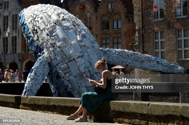 Tourist sits near a 12-metre installation depicting a whale, made up of five tons of plastic waste pulled out of the Pacific Ocean, is displayed in...